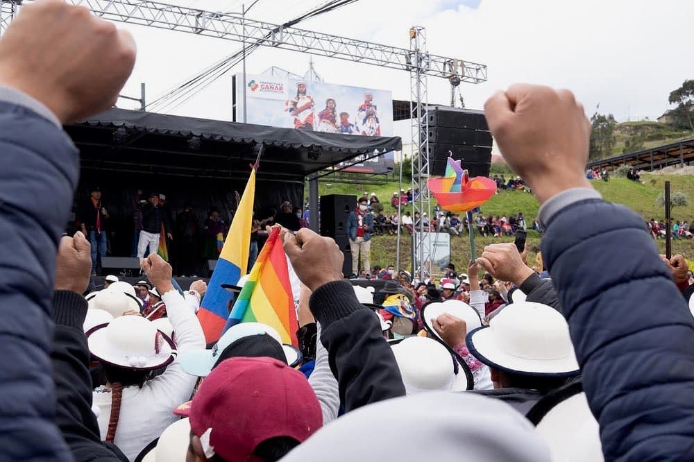 People in varied clothing in front of a stage, 
            facing a single speaker and cheering.